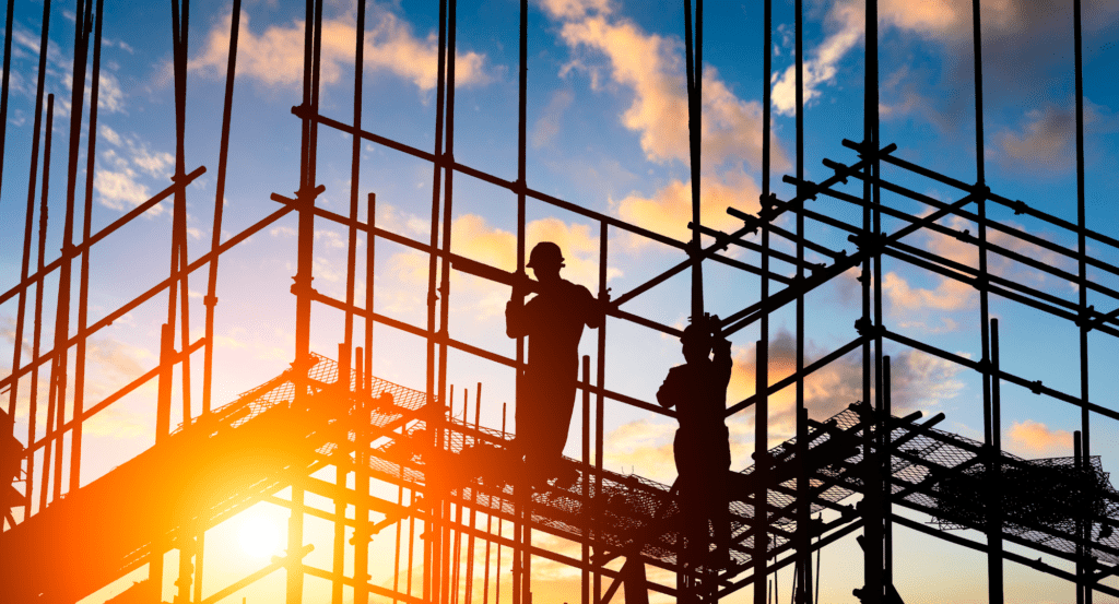 A silhouette of two construction workers standing on scaffolding.