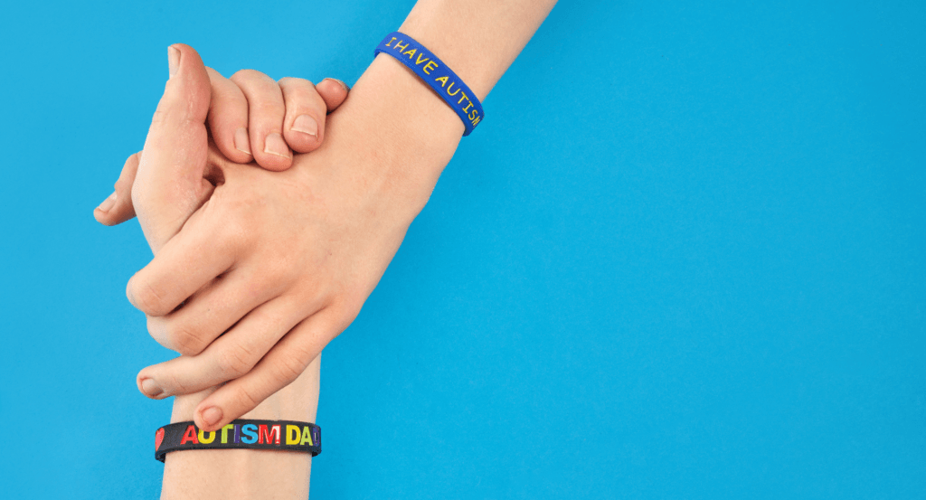 Blue background with two hands clasping each other, wearing Autism Awareness bracelets.